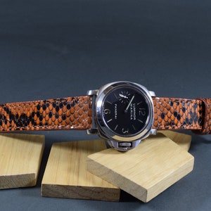 Może przedstawiać: Czarny i srebrny zegarek na rękę ze skórzanym paskiem w kolorze czarnym z wzorem skóry węża. Tarcza zegarka ma białe oznaczenia i tekst "Luminor Marina" oraz "Panerai".