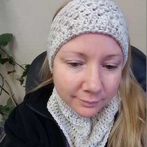 May include: A white crocheted headband and neck warmer set. The headband is wide and has a simple stitch pattern. The neck warmer is a cowl style and has a similar stitch pattern to the headband.