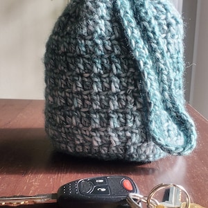 Könnte beinhalten: Eine teal- und graue gehäkelte Mütze mit einem Schlüsselanhänger mit einem Autoschlüssel, einem Flaschenöffner und mehreren Schlüsseln.