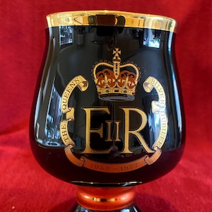 May include: Black ceramic goblet with gold trim and a gold design featuring the royal crest, the letters "ER", and the dates "1952-1977". The text "The Queen's Silver Jubilee" is also included in the design.