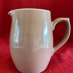 May include: A brown ceramic jug with a rounded body and a handle. The jug has a smooth, glossy finish.