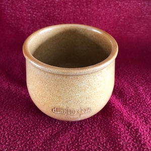 以下が含まれることがあります： 表面がざらざらした小さな茶色の陶器のカップ。カップは丸い底と広く開いた上部を持っています。カップの底には「Lancaster」という言葉が刻まれています。