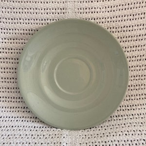 May include: A light green saucer with a slightly raised centre. The saucer is made of ceramic and has a smooth, glossy finish.