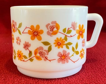 May include: White ceramic mug with a floral pattern in shades of orange, pink, and green. The flowers are stylized and have a retro look.