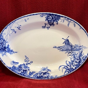 May include: Oval serving platter with a white base and blue floral and windmill design. The rim is decorated with a blue floral pattern. The platter features a landscape scene with a windmill and flowers.
