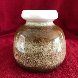 May include: A brown and white ceramic vase with a speckled glaze. The vase has a wide, round body and a white rim.