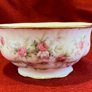 Könnte beinhalten: Eine weiße Porzellanschüssel mit goldfarbenem Rand und einem Blumenmuster aus rosa Rosen und grünen Blättern.