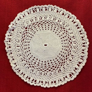 Pode incluir: Um tapete de crochê branco com um design circular e um padrão de renda delicado.