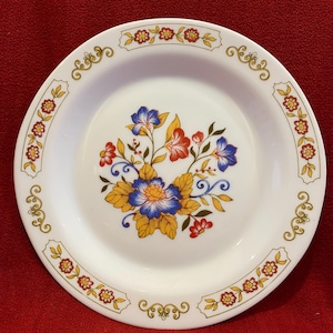 Puede incluir: Plato de cena de cerámica blanca con un diseño floral en tonos azules, amarillos, rojos y verdes. El plato tiene un borde dorado con un patrón floral repetitivo.