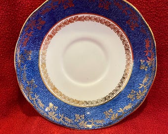 May include: A blue and gold saucer with a white center. The saucer has a gold rim and a floral design.