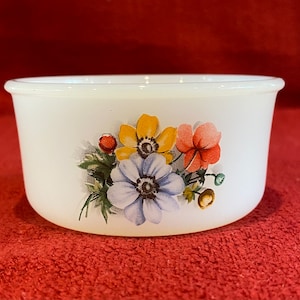 May include: White ceramic bowl with a floral design featuring yellow, blue, and red flowers. The bowl has a smooth, rounded rim.