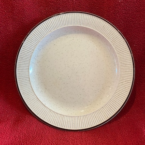May include: A white ceramic dinner plate with a brown rim and a speckled design. The plate has a raised, fluted edge.