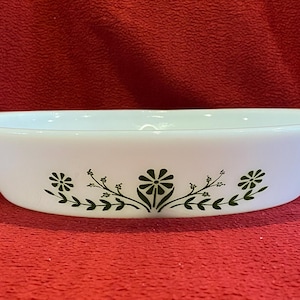 May include: White oval baking dish with a green floral design. The dish has a slightly raised rim.