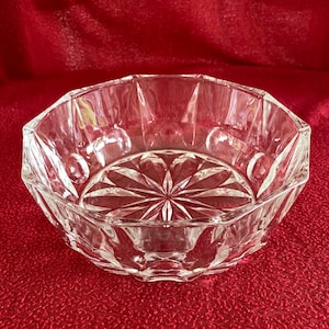 Puede incluir: Un cuenco de vidrio transparente con un diseño geométrico. El cuenco tiene un patrón de estrella en el centro y un borde festoneado.