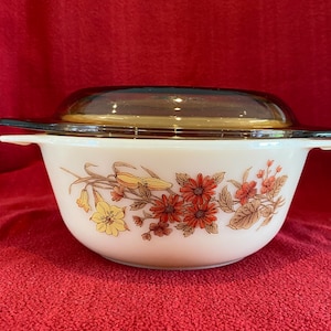 May include: A white casserole dish with a brown lid. The dish has a floral pattern with red, yellow, and brown flowers.