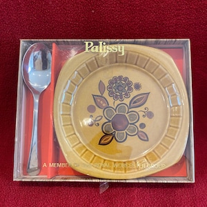 Könnte beinhalten: Ein Set in einer Schachtel mit einem kleinen, gelben Teller mit Blumenmuster und einem silbernen Löffel. Die Schachtel ist mit "Palisssy" und "A Member of the Royal Worcester Group" beschriftet.