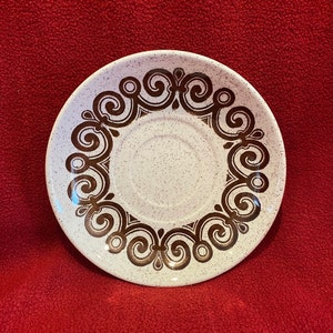 May include: White saucer with a brown swirl design around the edge.