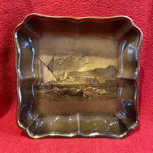 May include: A decorative, scalloped-edge tray with a gold rim. The tray features a sepia-toned illustration of a coastal scene with sailboats, buildings, and the text "The Bay of Naples".
