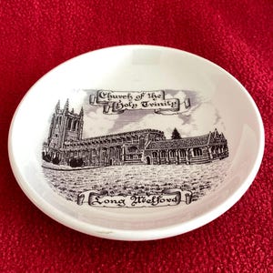 May include: A white, round decorative dish with a black and white illustration of a church. The text "Church of the Holy Trinity" and "Long Melford" are displayed on the dish.