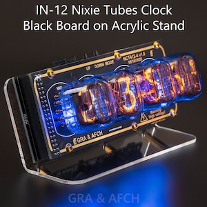 Pode incluir: Um relógio IN-12 Nixie Tubes preto e dourado com um quadro negro e um suporte de acrílico. O relógio mostra a hora 10:30:20. O relógio tem um rótulo de advertência que diz "Aviso! Alta tensão!"