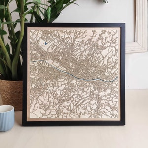 May include: A wooden map of a city with a river running through it. The map is laser cut and has a black frame.