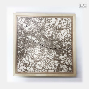 May include: A wooden map of a city, laser cut and mounted in a light wood frame. The map is detailed and shows the streets and buildings of the city.