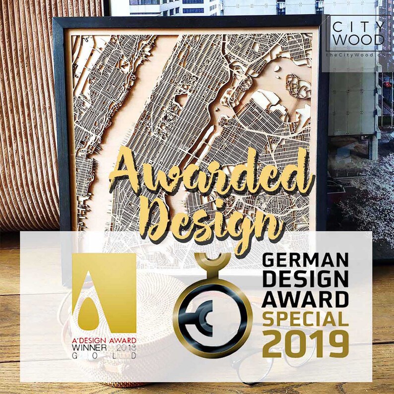May include: A wooden map of a city with the text "Awarded Design" in gold lettering. The map is framed in black and has a gold award seal with the text "German Design Award Special 2019".