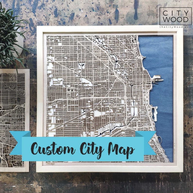 May include: A custom wooden city map of Chicago, laser cut and framed in a white frame. The map is mounted on a blue background. The text "Custom City Map" is displayed on a blue ribbon.