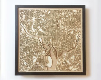 Op de afbeelding: Een lasergesneden houten kaart van Washington, D.C. in een zwart frame. De kaart toont de straten en waterwegen van de stad in detail.
