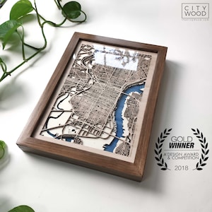 May include: A framed wooden map of Philadelphia, Pennsylvania, with a blue water feature. The frame is made of dark wood and has a gold "Gold Winner" award sticker with the text "A' Design Award & Competition 2018".