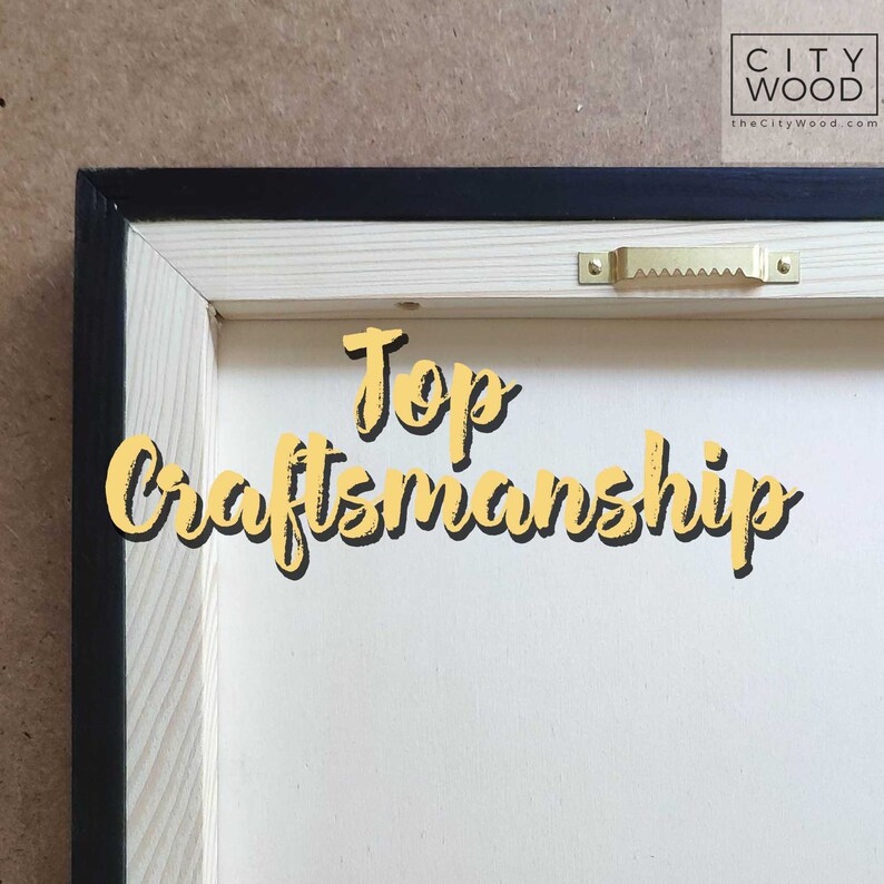 May include: Close-up of the back of a wooden frame with a black border. The frame is made of natural wood and has a gold-colored hanging hook. The text "Top Craftsmanship" is written in yellow on the frame.