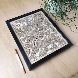 Pode incluir: Um mapa de madeira de Munique, Alemanha, emoldurado em preto. O mapa é cortado a laser e mostra as ruas e os marcos da cidade.