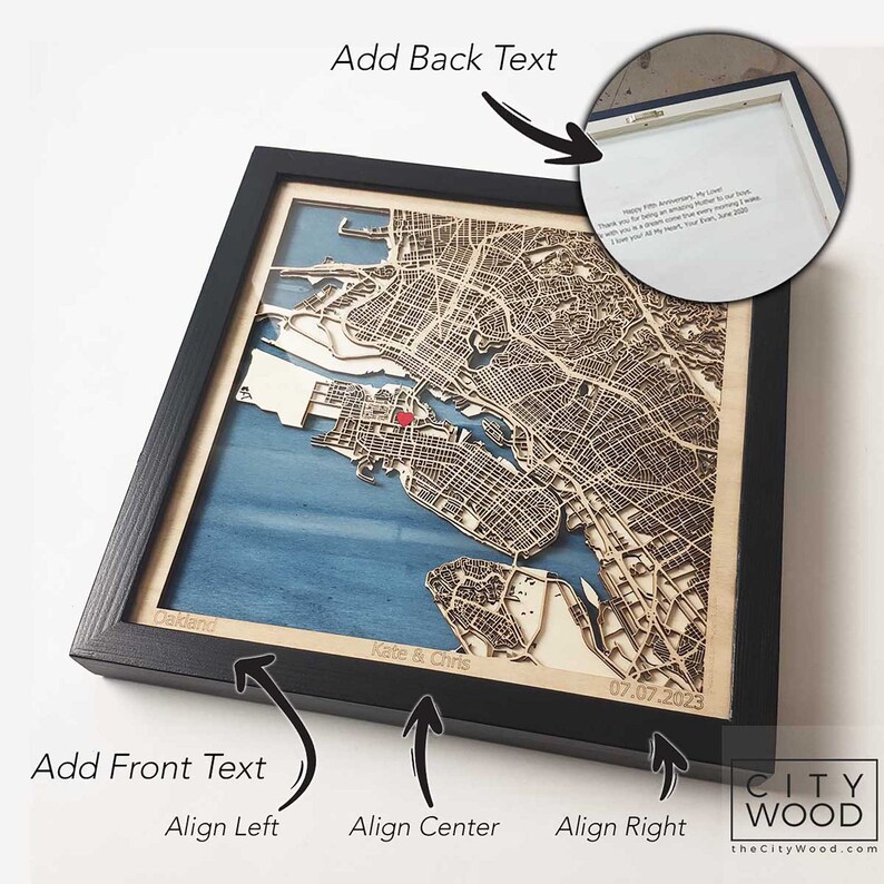 May include: A framed wooden map of Oakland, California with a blue background. The map is laser cut and has a 3D effect. The frame is black and the map is personalized with the text "Kate & Chris" and the date "07.07.2023".