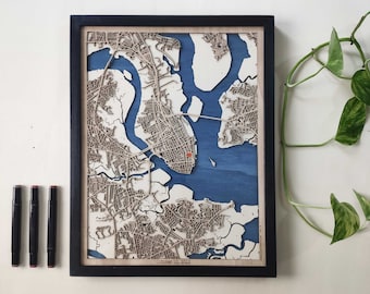 May include: A wooden map of a city with a blue water feature. The map is framed in black and has the date "October 10, 2022" printed on the bottom.