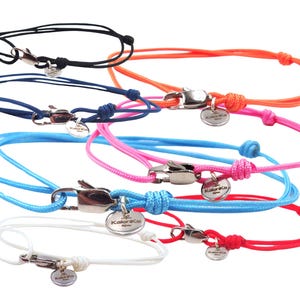 Peut inclure: Collection de bracelets en cordon colorés. Chaque bracelet est doté d'un fermoir argenté et d'un petit charme rond. Les bracelets sont disponibles en noir, orange, bleu, rose, bleu clair, blanc et rouge.
