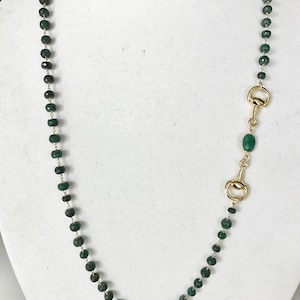 May include: A long green gemstone necklace with gold accents. The necklace features a gold clasp and a green gemstone pendant.