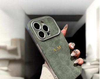 Op de afbeelding: Een groene telefoonhoes met een zilveren frame en camerabehuizing. De hoes heeft een getextureerde afwerking en is voorzien van de geborduurde initialen "A.M" in goud. De hoes is ontworpen voor een smartphone.