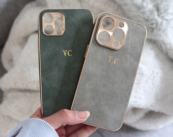 Op de afbeelding: Twee telefoonhoesjes met gouden accenten en een suède-achtige textuur. Het hoesje aan de linkerkant is groen met de initialen "VC" in gouden letters. Het hoesje aan de rechterkant is grijs met de initialen "T.C" in gouden letters.
