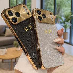 以下が含まれることがあります： 黒とシルバーのグリッター仕上げの携帯電話ケース2つ。各ケースは、金色のカメラフレームと、金色のイニシャル「R.S」と「S.H」を備えています。ケースはデザインを示すために持ち上げられています。