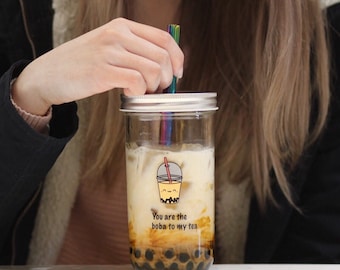 May include: A clear glass jar with a silver lid filled with brown boba tea. The jar has a white sticker with the text "You are the boba to my tea" and a cartoon image of a boba tea cup with a smiling face.