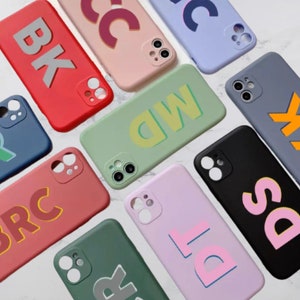 May include: Assortment of colorful phone cases with different letter designs. The cases are made of silicone and have a matte finish. The letters are raised and have a 3D effect. The cases are available in a variety of colors, including pink, blue, green, red, and black.