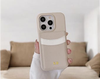 May include: A beige phone case with a white pocket and the initials "S.B." in gold lettering.