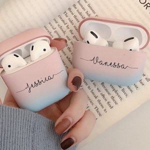 Könnte beinhalten: Zwei rosa und blaue Airpod-Hüllen mit den Namen "Jessica" und "Vanessa" in schwarzer Schrift.