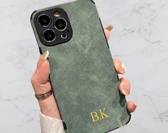 Op de afbeelding: Een groene suède telefoonhoes met een zwarte uitsparing voor de camera lens en de initialen "B.K." in gouden letters.