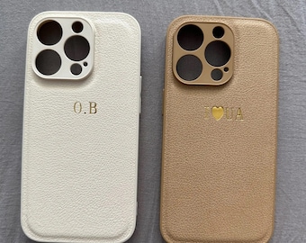 May include: Two phone cases, one white and one brown, with a raised camera bump and a gold inscription. The white case says "O.B." and the brown case says "I ♥ UA".
