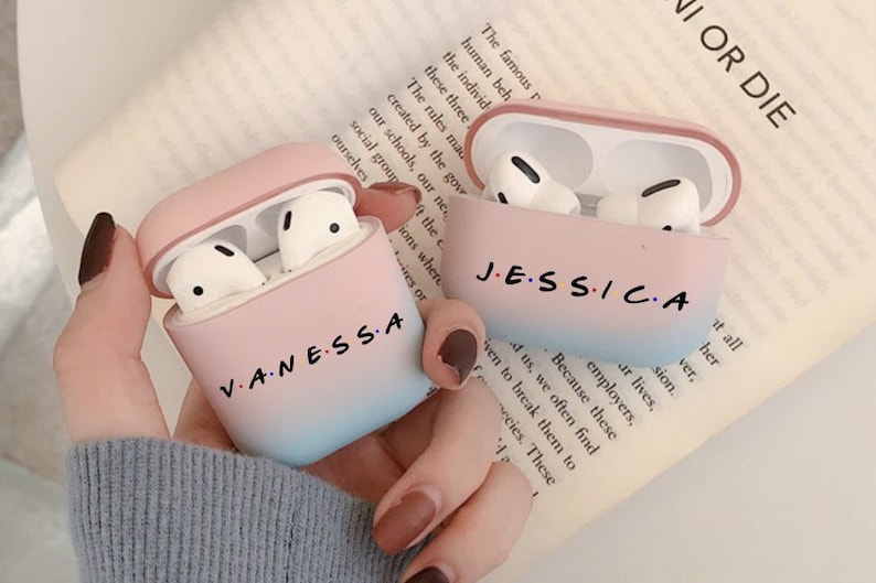 May include: Two pink and blue gradient Airpods cases with the names "Vanessa" and "Jessica" printed on them in black.
