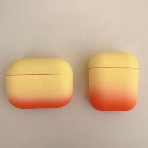 May include: Two yellow and orange gradient AirPod cases. The cases are made of a soft, rubbery material and have a smooth finish.