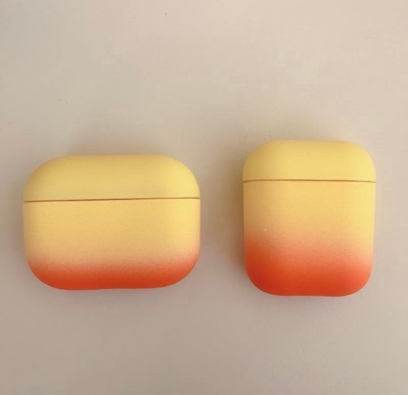 May include: Two yellow and orange gradient AirPod cases. The cases are made of a soft, rubbery material and have a smooth finish.