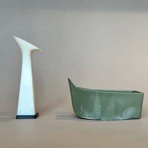 May include: Two 3D printed objects, one white and one green. The white object is tall and slender, resembling a tower. The green object is shorter and wider, resembling a boat.