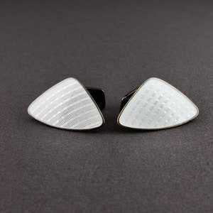 May include: A pair of white enamel cufflinks in the shape of a triangle with a geometric pattern.